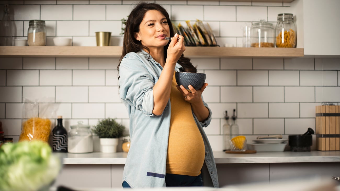 Happy pregnant woman eating breakfast from a bowl
