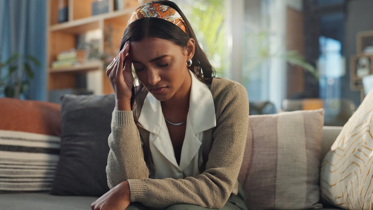 Sick, woman and headache on sofa in home for health problem, fatigue and low blood pressure of anemia. Frustrated, tired and person with migraine in living room for vertigo, dizzy and iron deficiency
