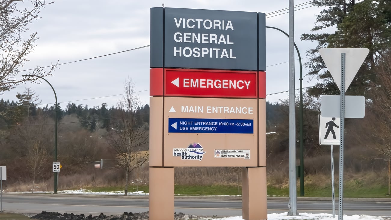Victoria General Hospital's exterior signage under an overcast sky directs patients to the Emergency and Main Entrance, including after-hours instructions.