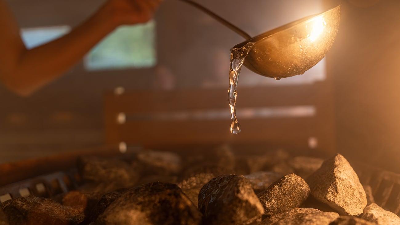 A ladle of water being poured on rocks in a sauna