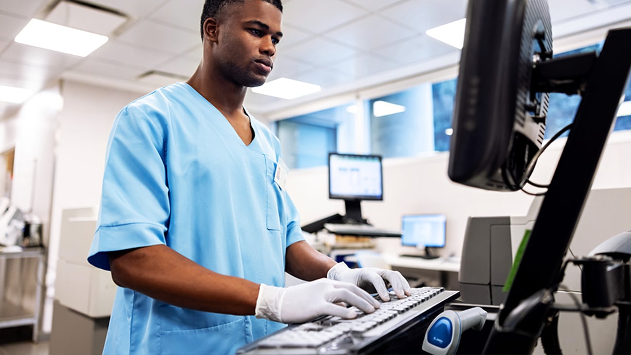 Healthcare worker in scrubs typing on keyboard.
