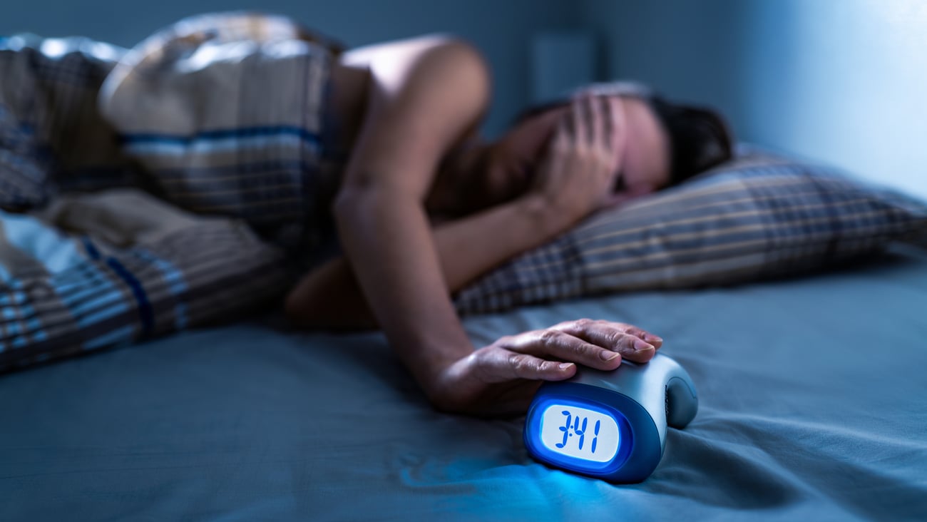 Young woman holding her hand over her eyes, distressed by not being able to sleep