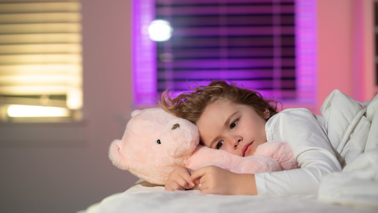 A young girl with brown hair in bed with her pink teddy bear