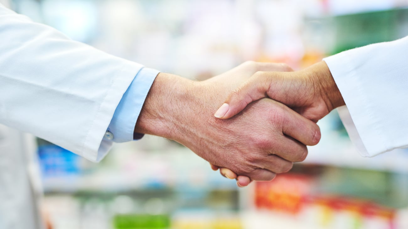 Two pharmacists shake hands at a pharmacy.