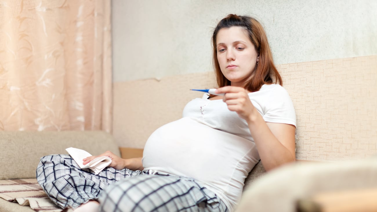 Young pregnant woman checking her temperature with a thermometre
