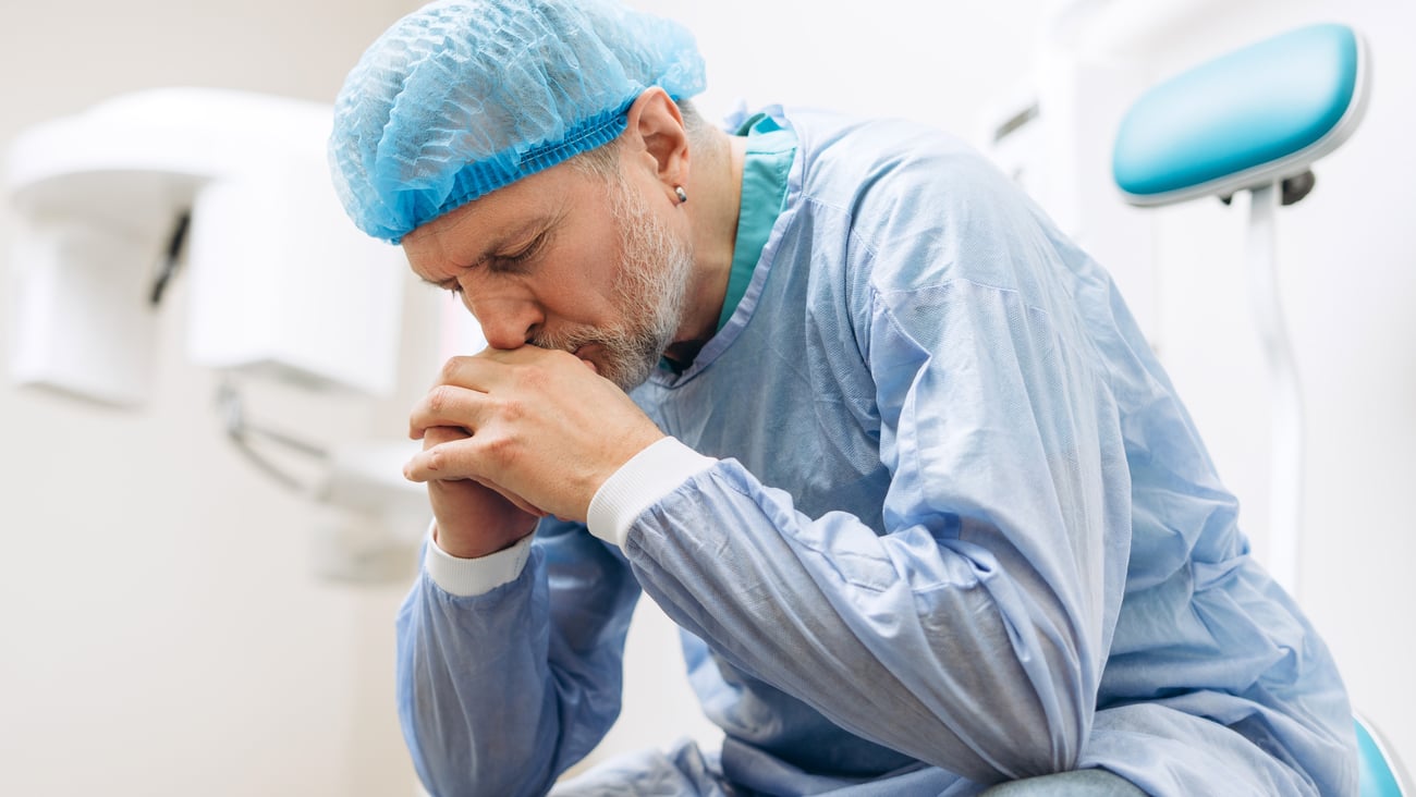 white male surgeon sitting with hands on chin, looking stressed