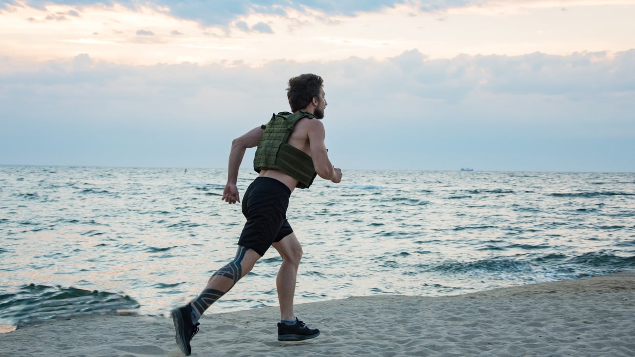 Young man running along the beach wearing a weighted vest