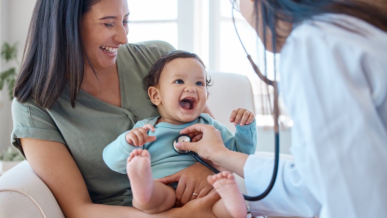 Family doctors listening to the heartbeat of a happy toddler being held by the mom