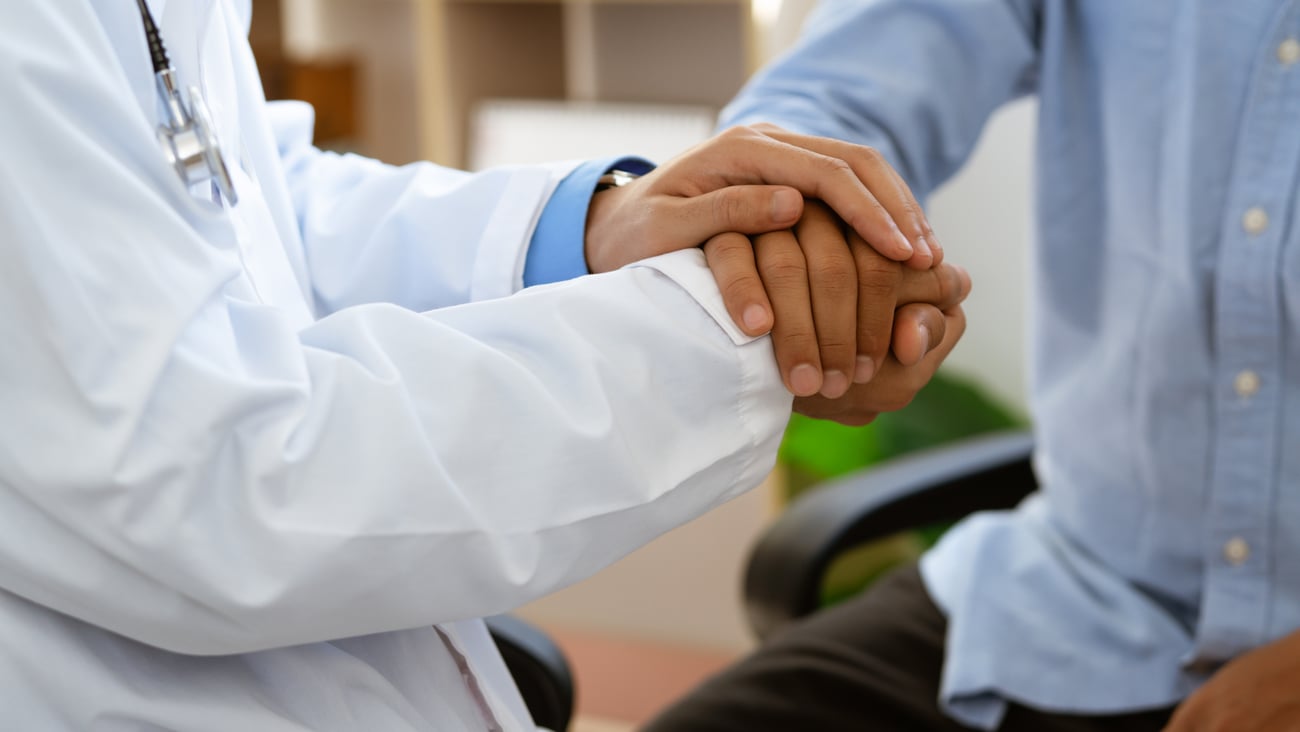 Caring doctor in white coat holding hands of man patient express compassion provide physical or psychological help, arms close up.