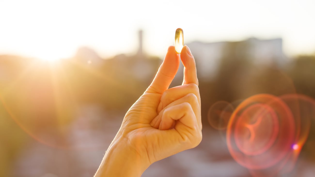 A woman's hand holding a vitamin capsule in the bright sunlight