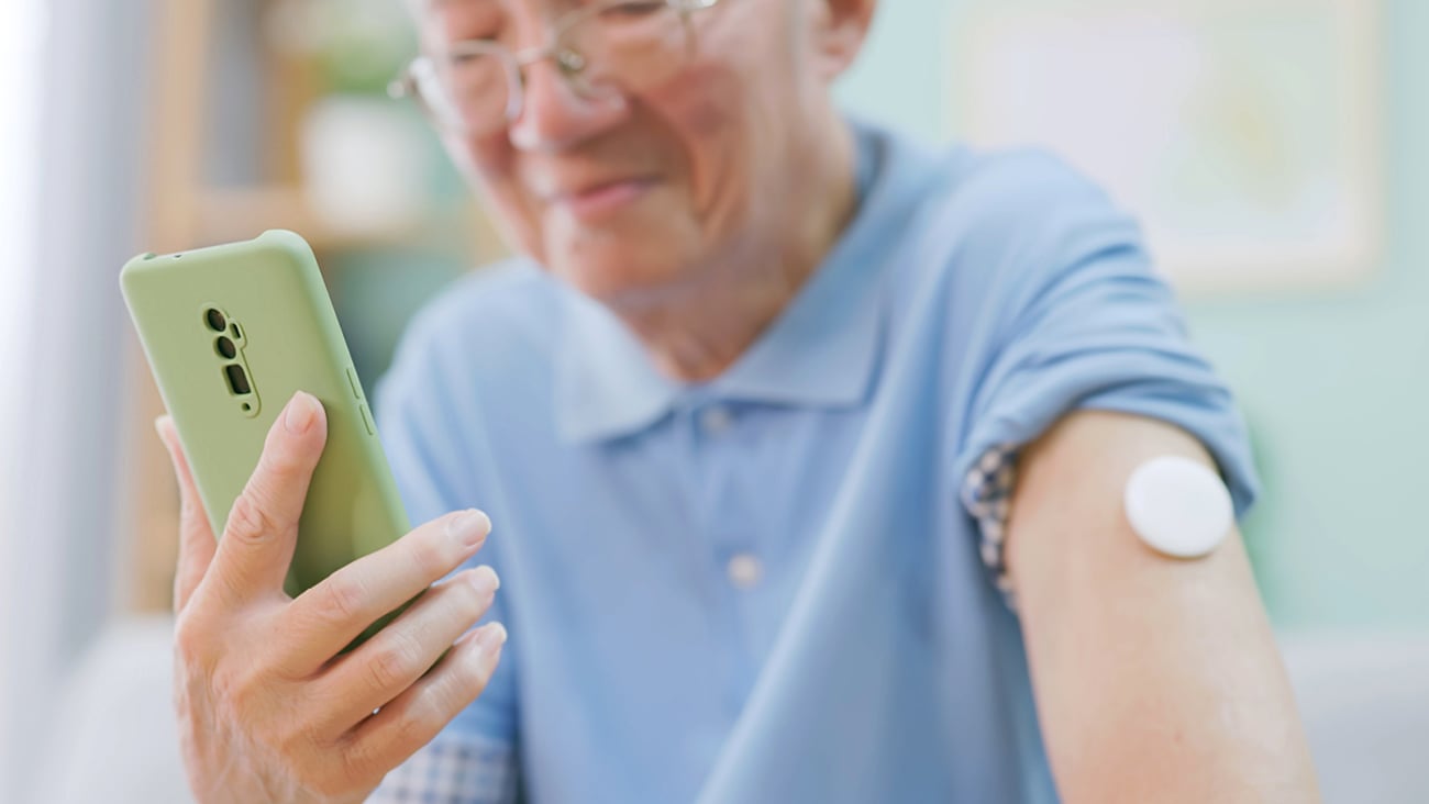 Older Asian male patient with a CGM on his arm checking his phone
