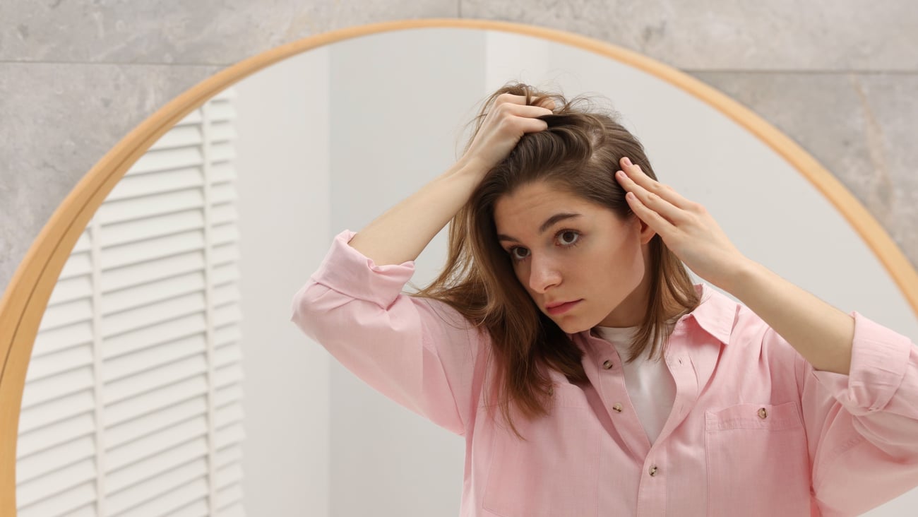 Young woman examining her scalp in the mirror, worried she is losing her hair
