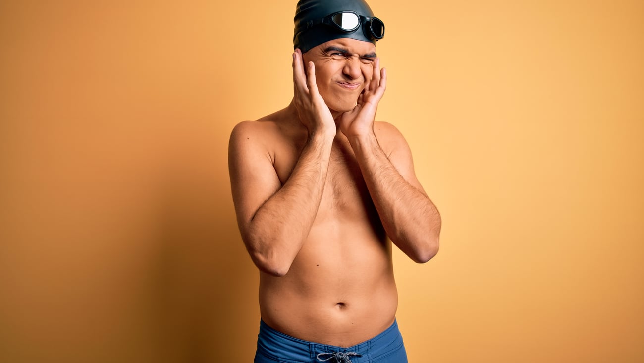 A young male swimmer in a bathing cap and goggles with sore ear