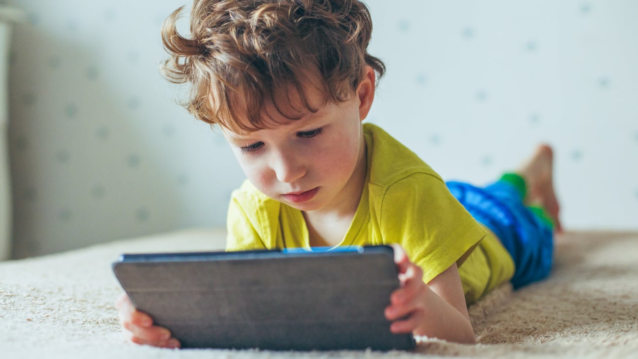 A young boy watching a tablet while laying on his stomach