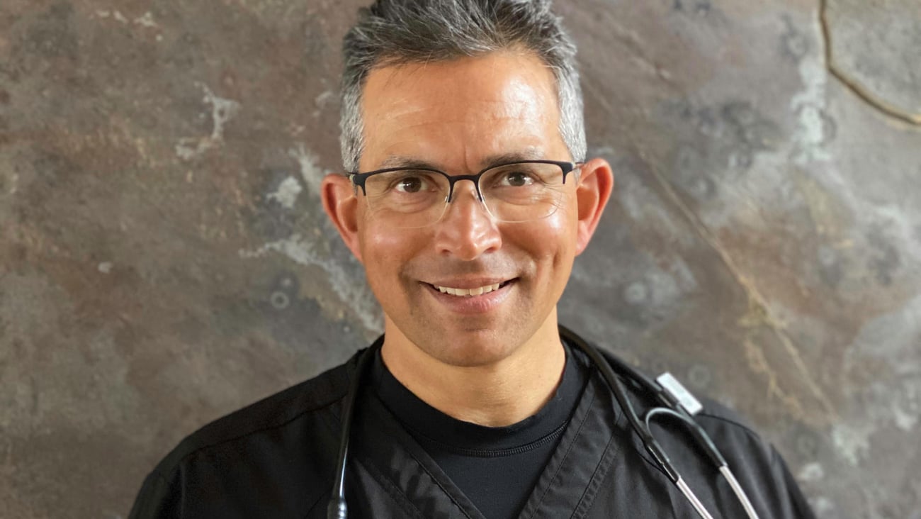 Smiling male doctor in a black shirt with a stethoscope around his neck