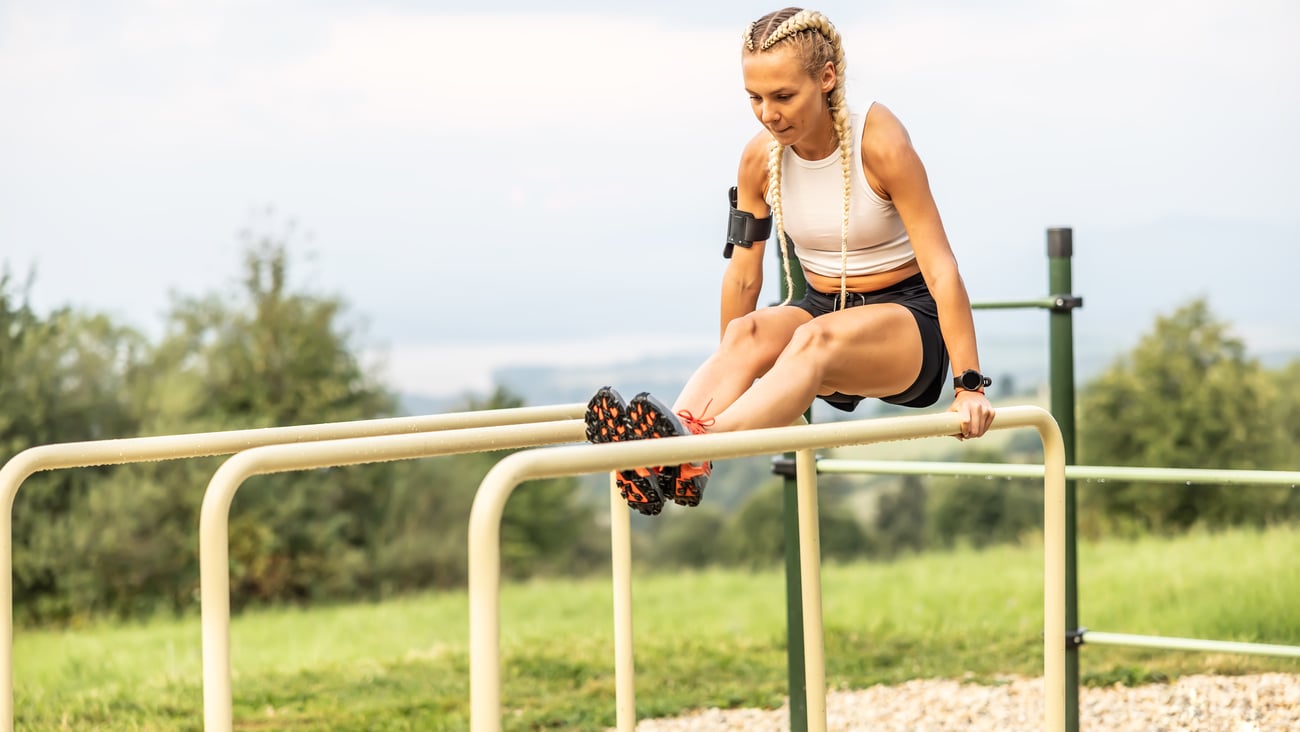 Younger white woman with blonde braids working out at an outdoor set of bars