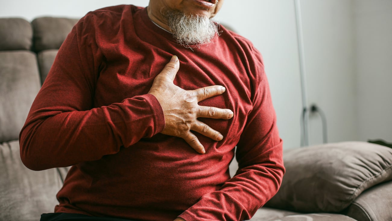 Older man in a red shirt clutching his chest in pain