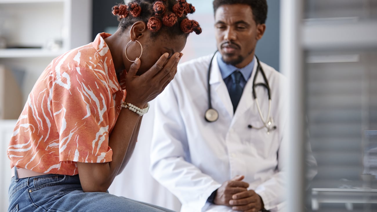 Black male doctor with crying Black female patient