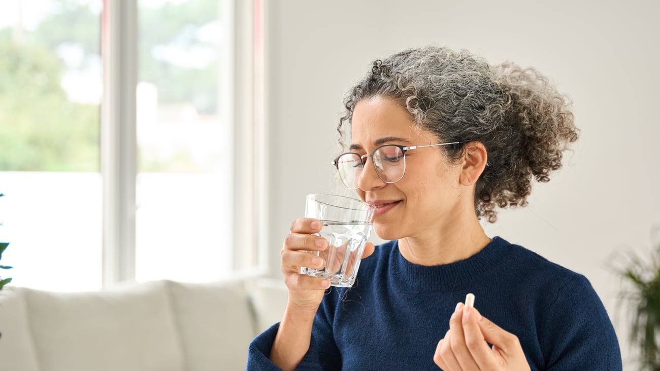 Older woman with glasses taking a white pill