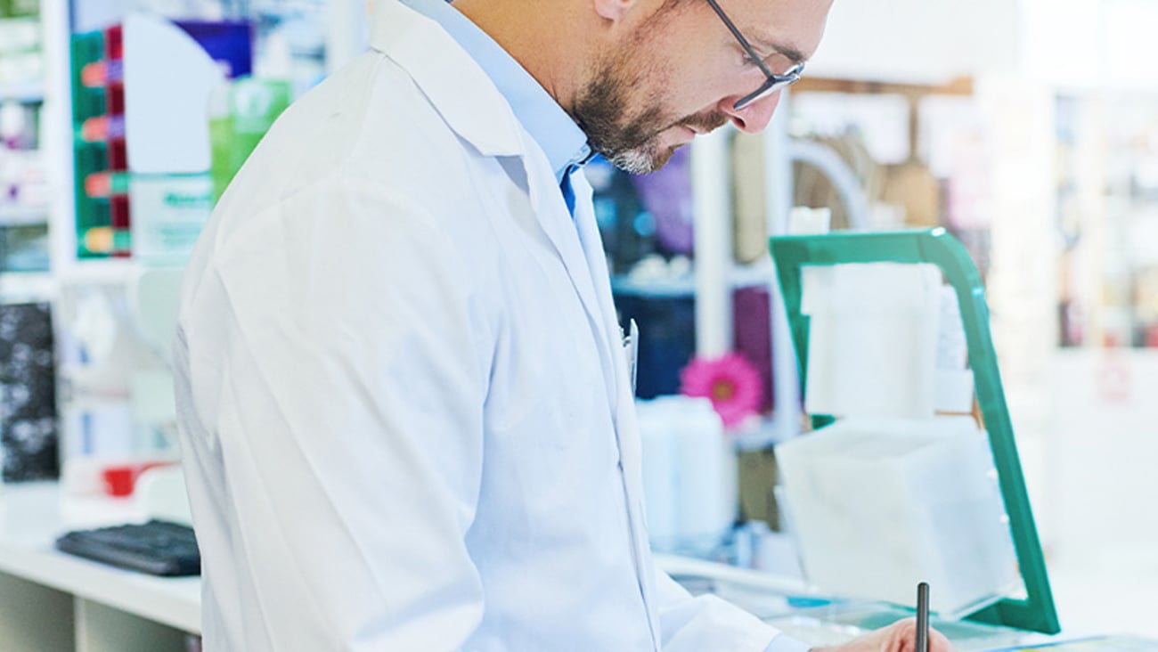 male pharmacist looks down on forms he is signing at the pharmacy counter