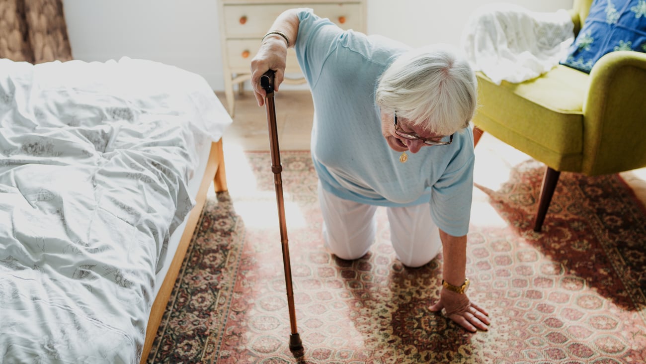 Elderly woman, white, white hair, by bed, on knees, has fallen, holding cane