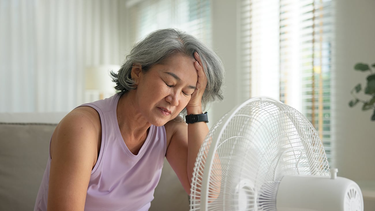Woman in front of fan, looking fatigued.