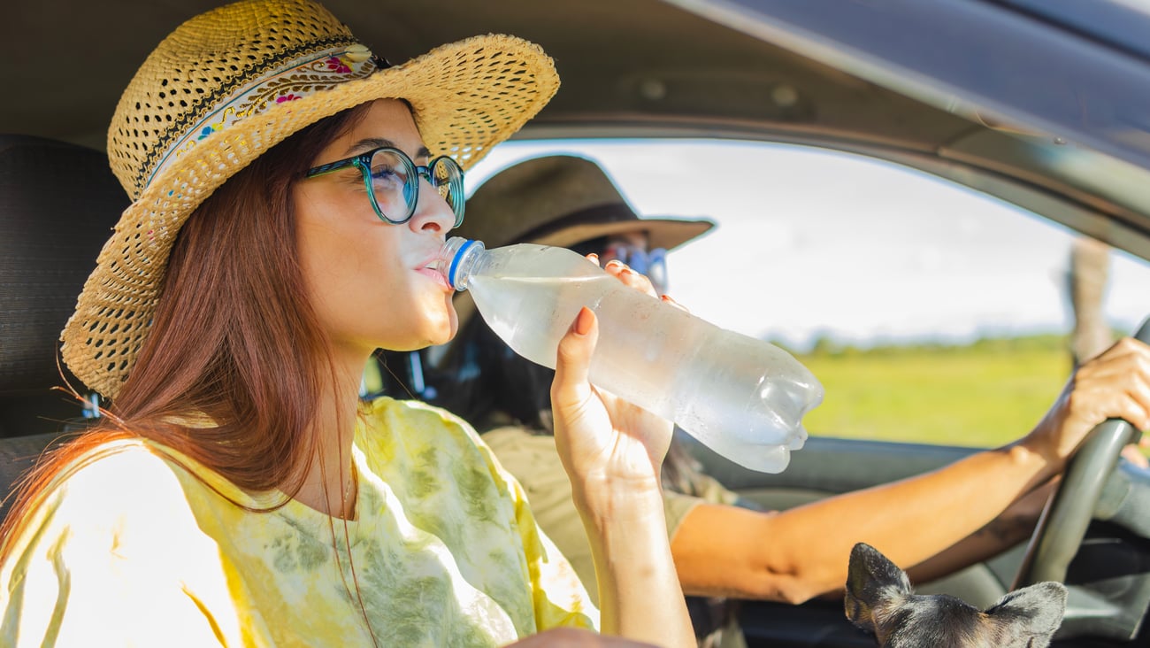 A man and  woman in a car in hot sun drinking water from bottle