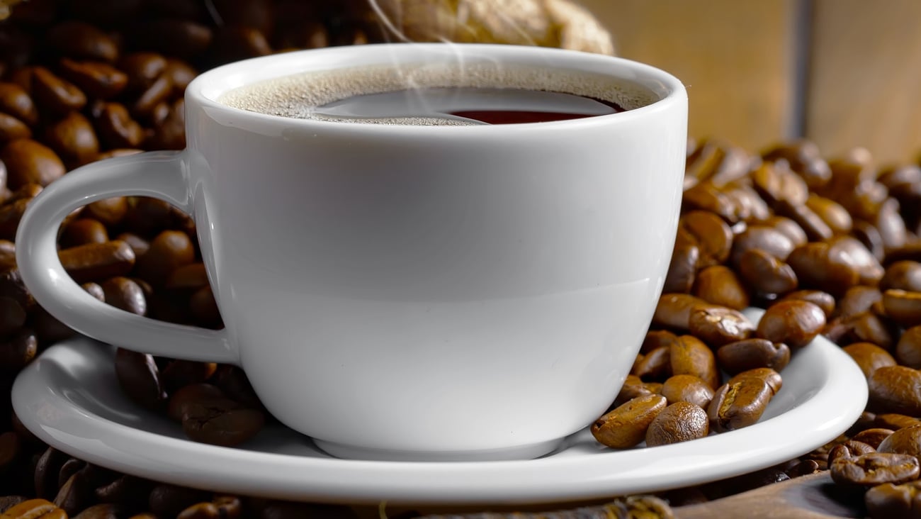 coffee in white porcelain cup sitting on a blanket of coffee beans.