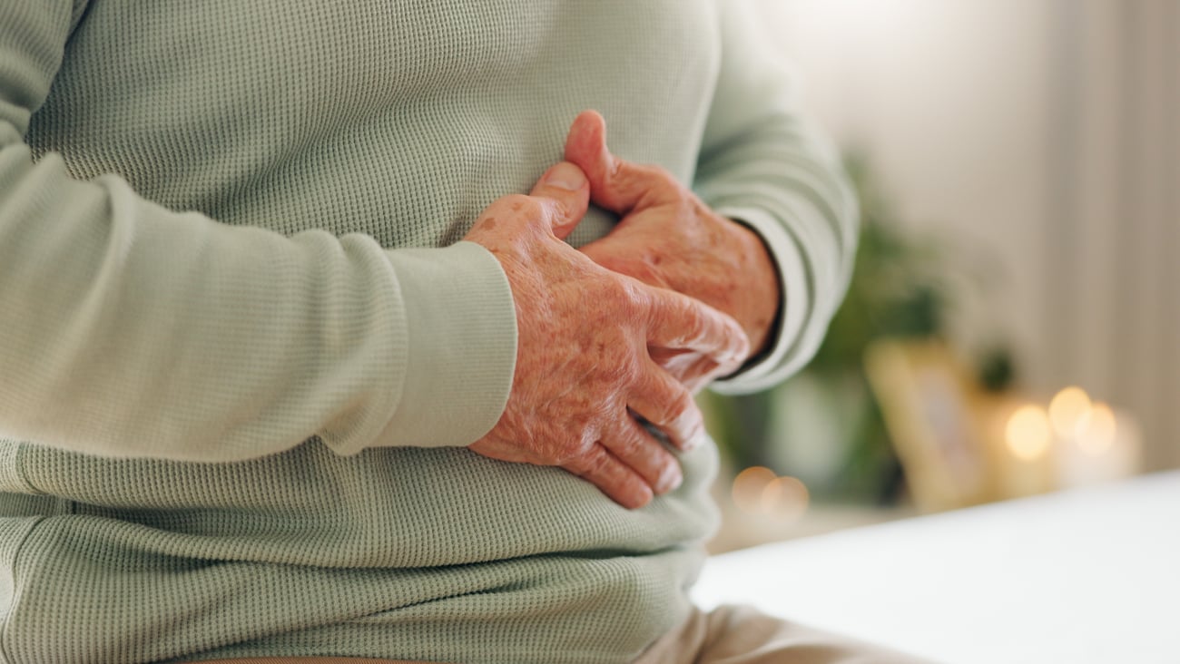Older person holding their stomach because it hurts wearing a green sweater