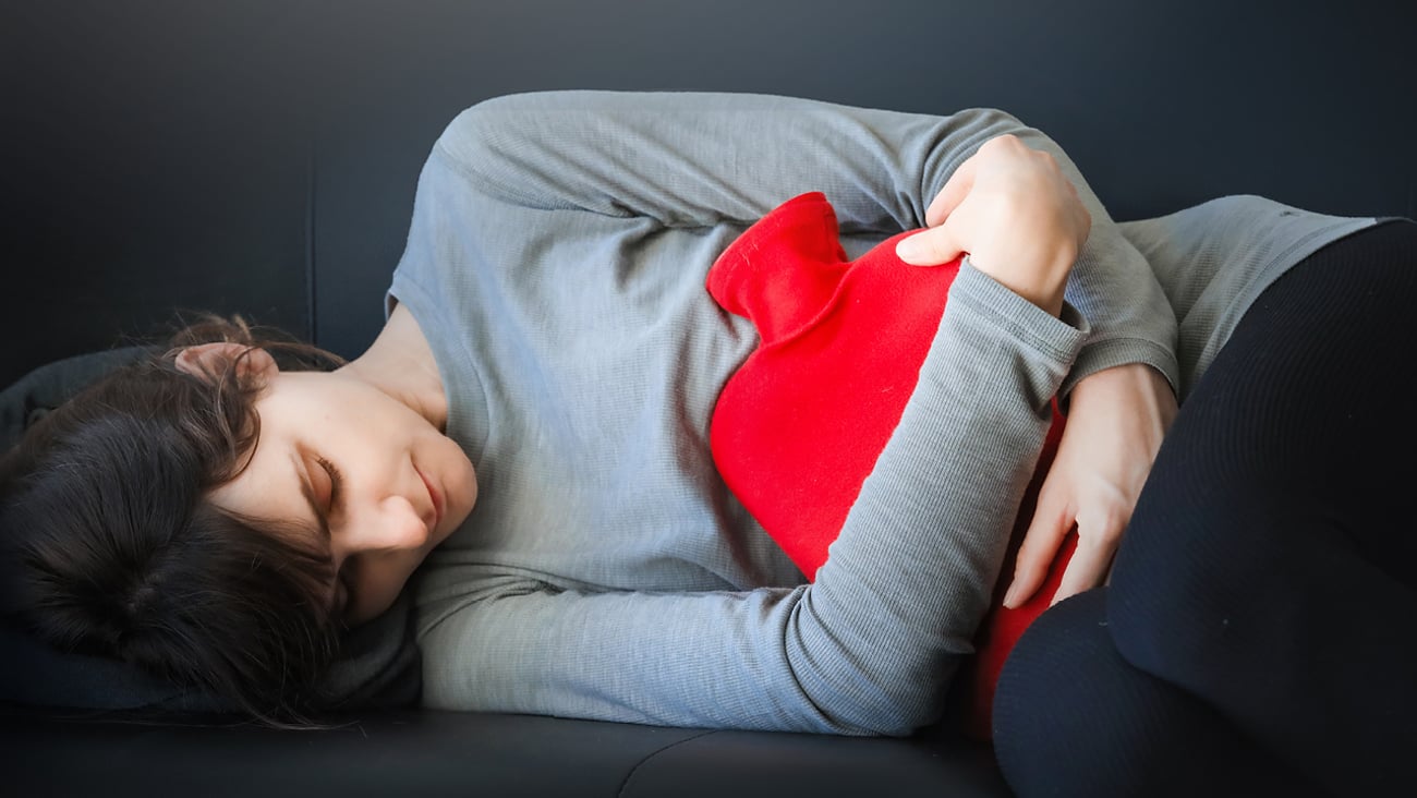 Teenager holding a hot water bottle to their stomach 