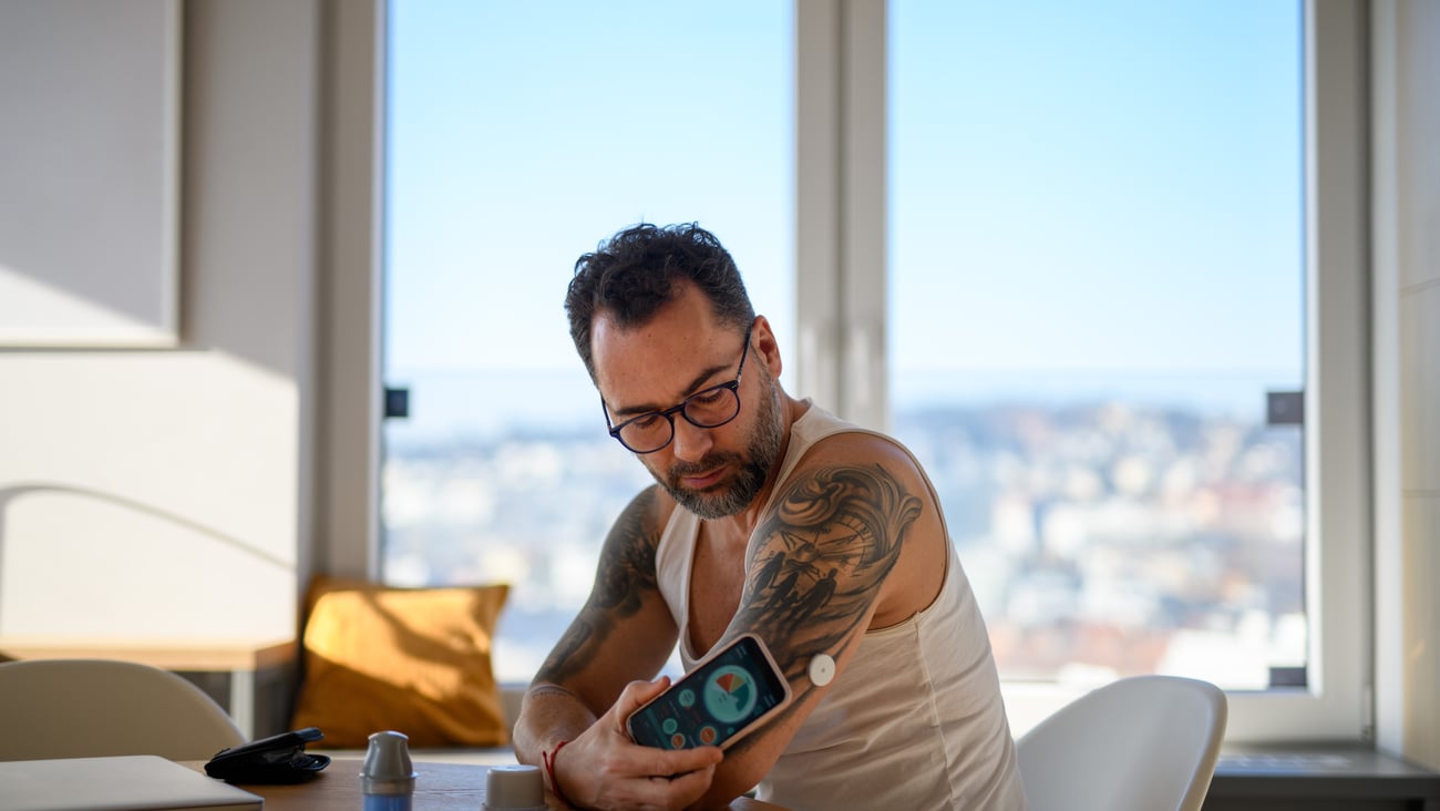 Tatooed white man checking his blood sugar with a continuous glucose monitor