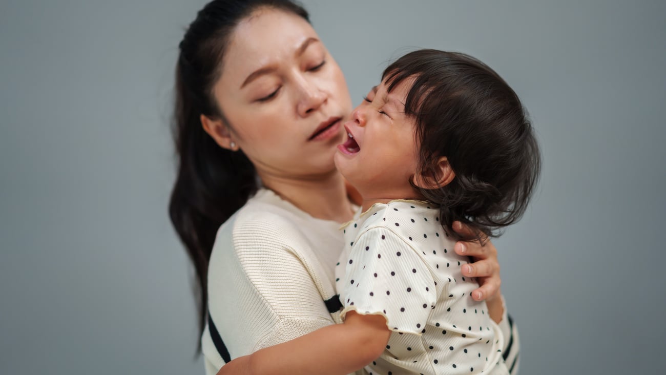 A young Asian child crying in pain being comforted by the mother