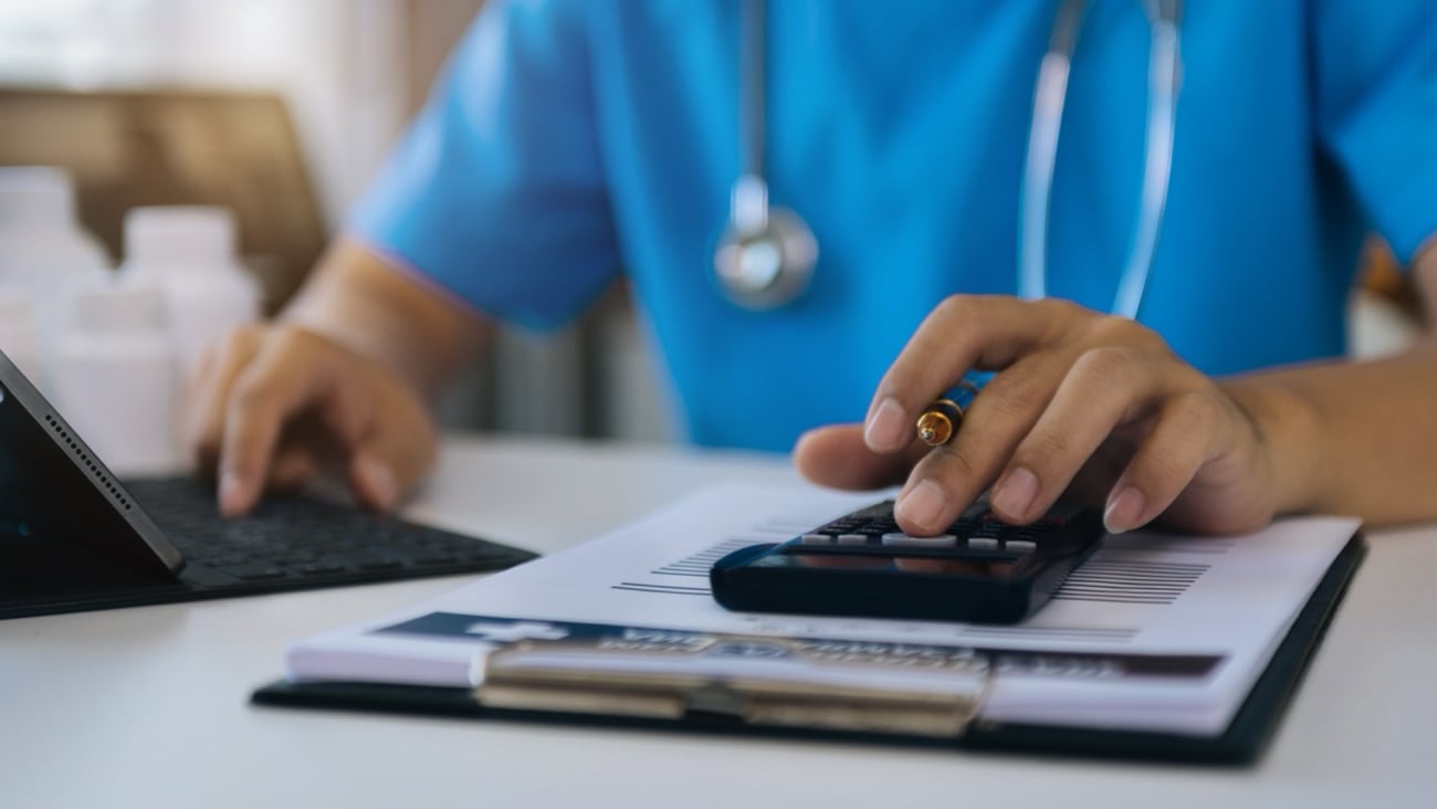 A doctor wearing a stethoscope uses a calculator.