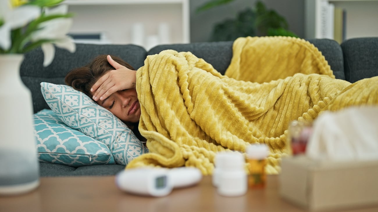 Young woman sick on the couch under a yellow blanket