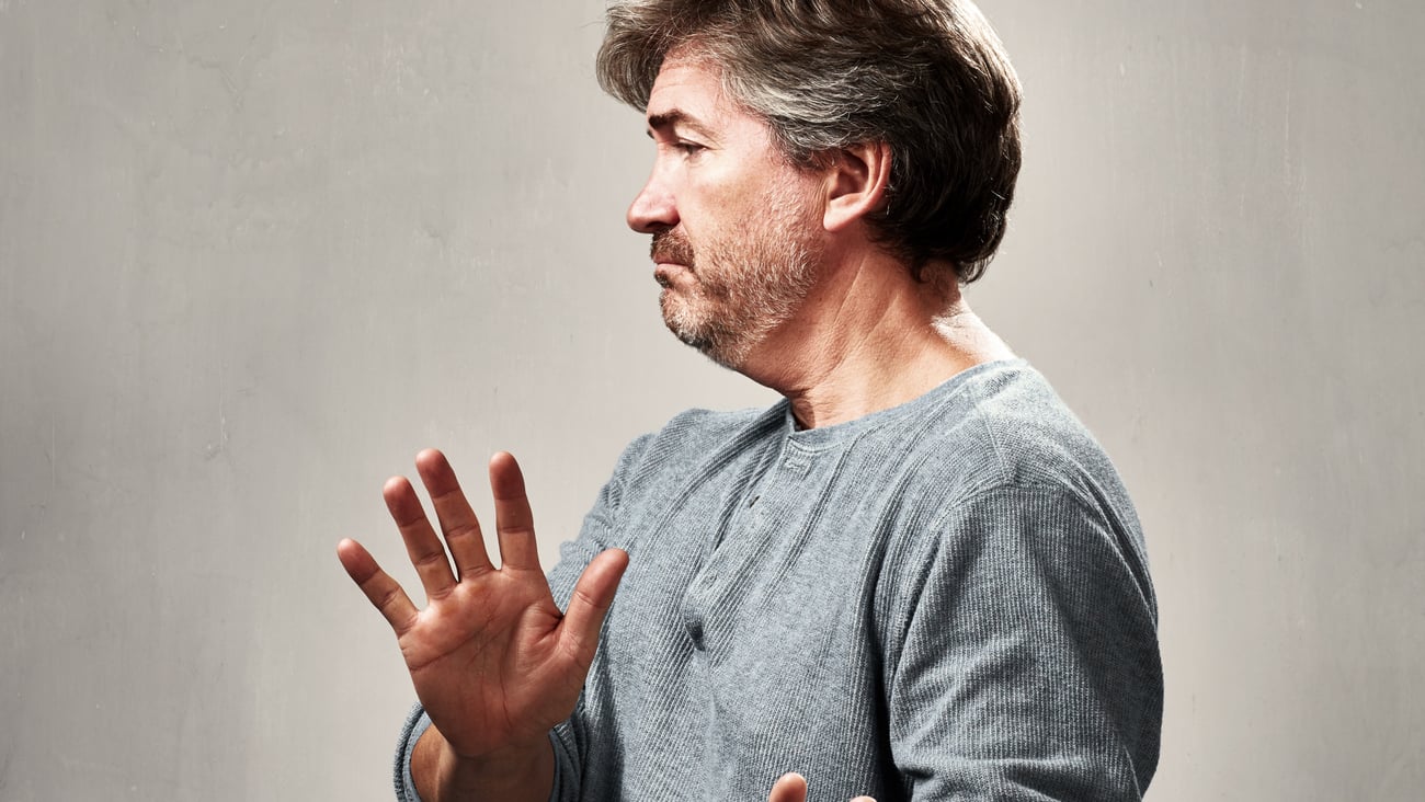 A gray-haired white man pushing away someone with his hands