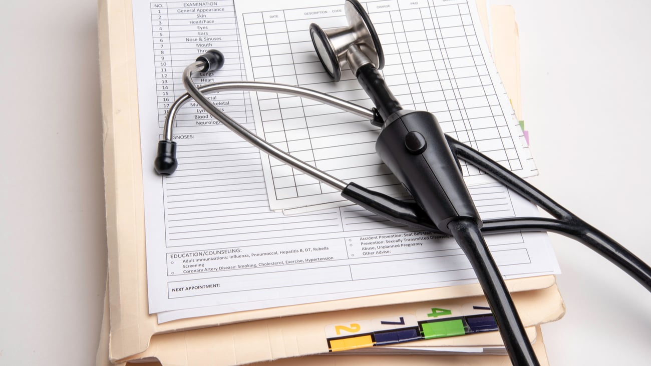 A stack of medical records underneath a stethoscope. 