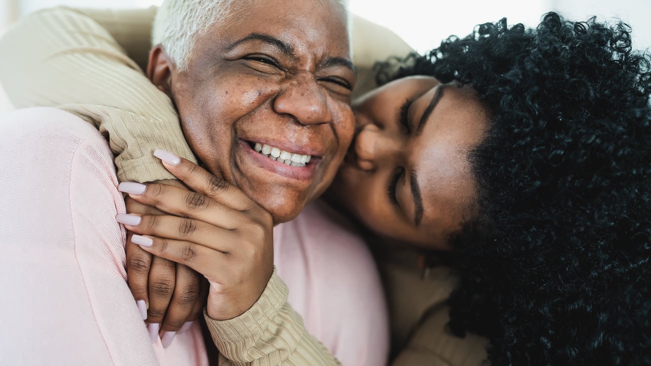 Adult daughter giving her older mother a hug and kiss