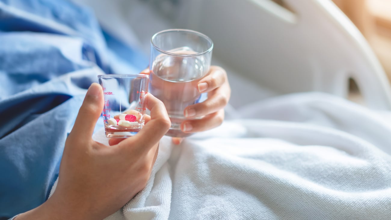 Patient with drugs in a cup ready to take them laying down in a hospital bed