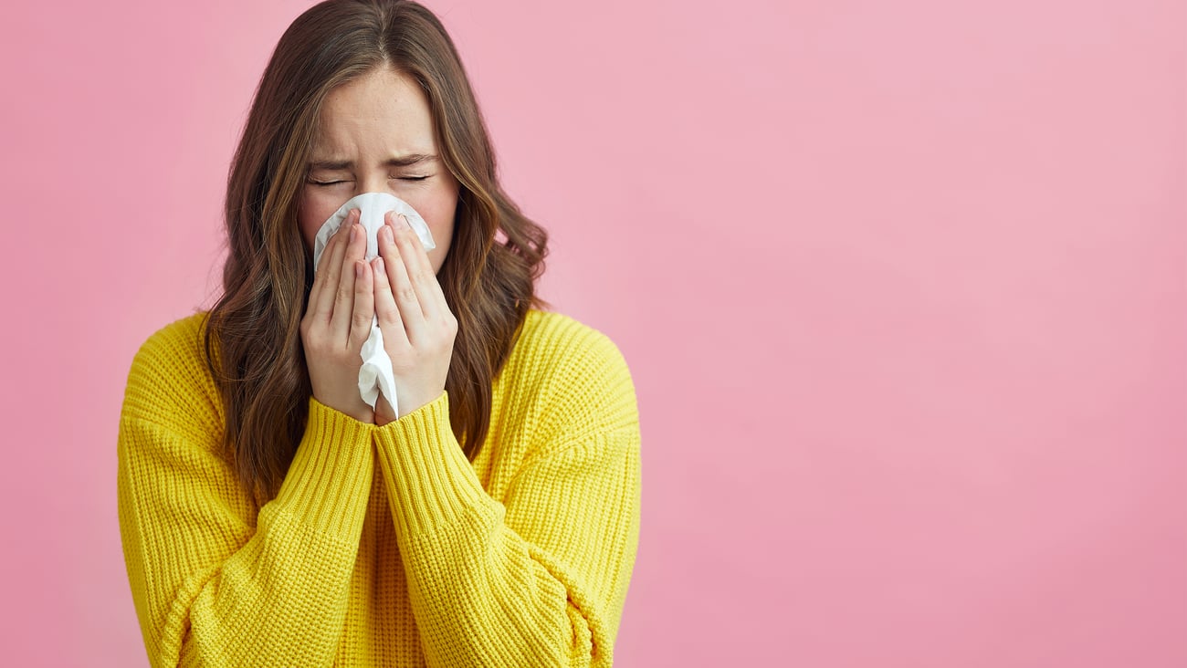 Young white woman in a yellow sweater blowing her nose