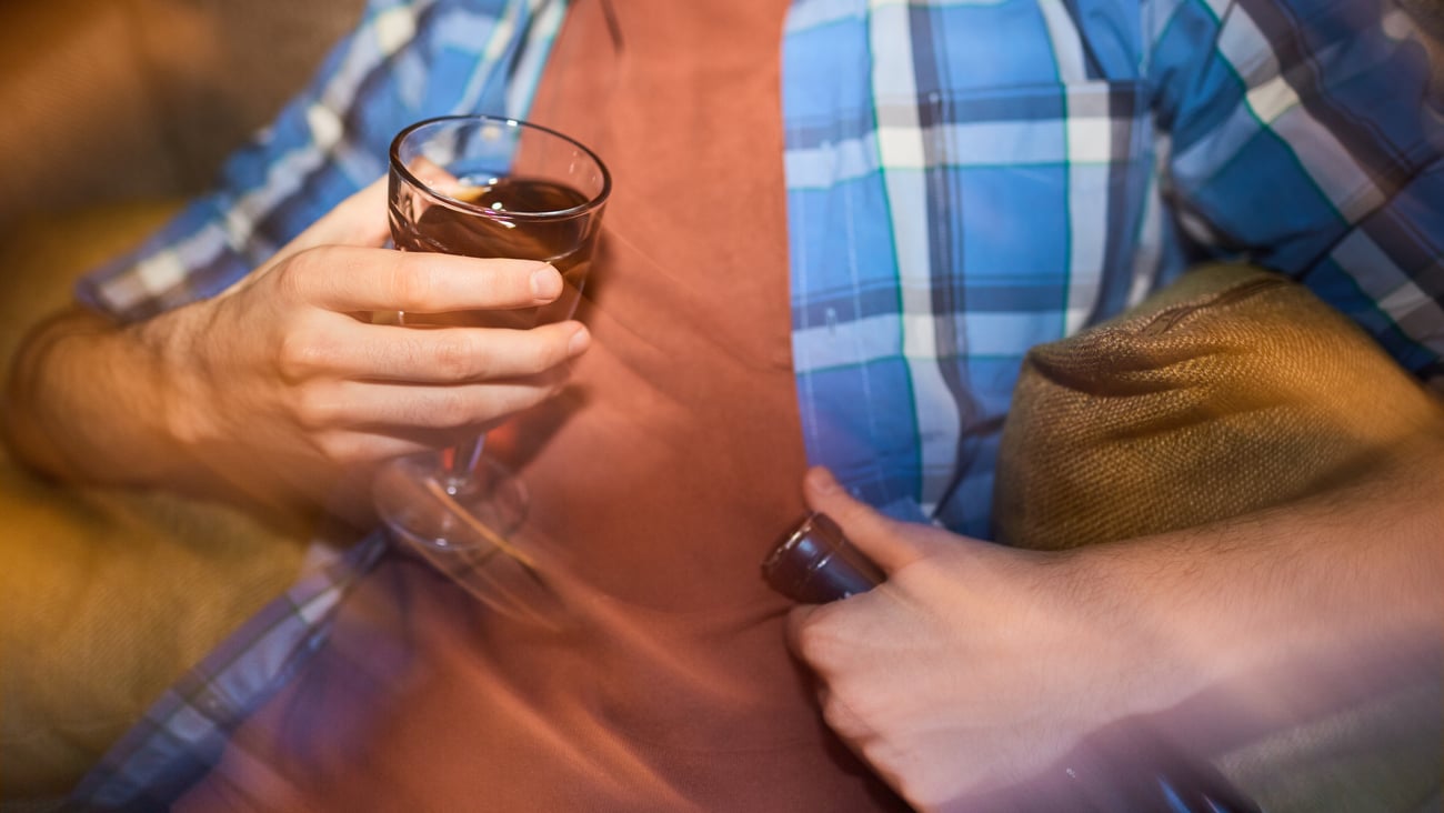 Close up of man's torso as he clutches a drink to his chest