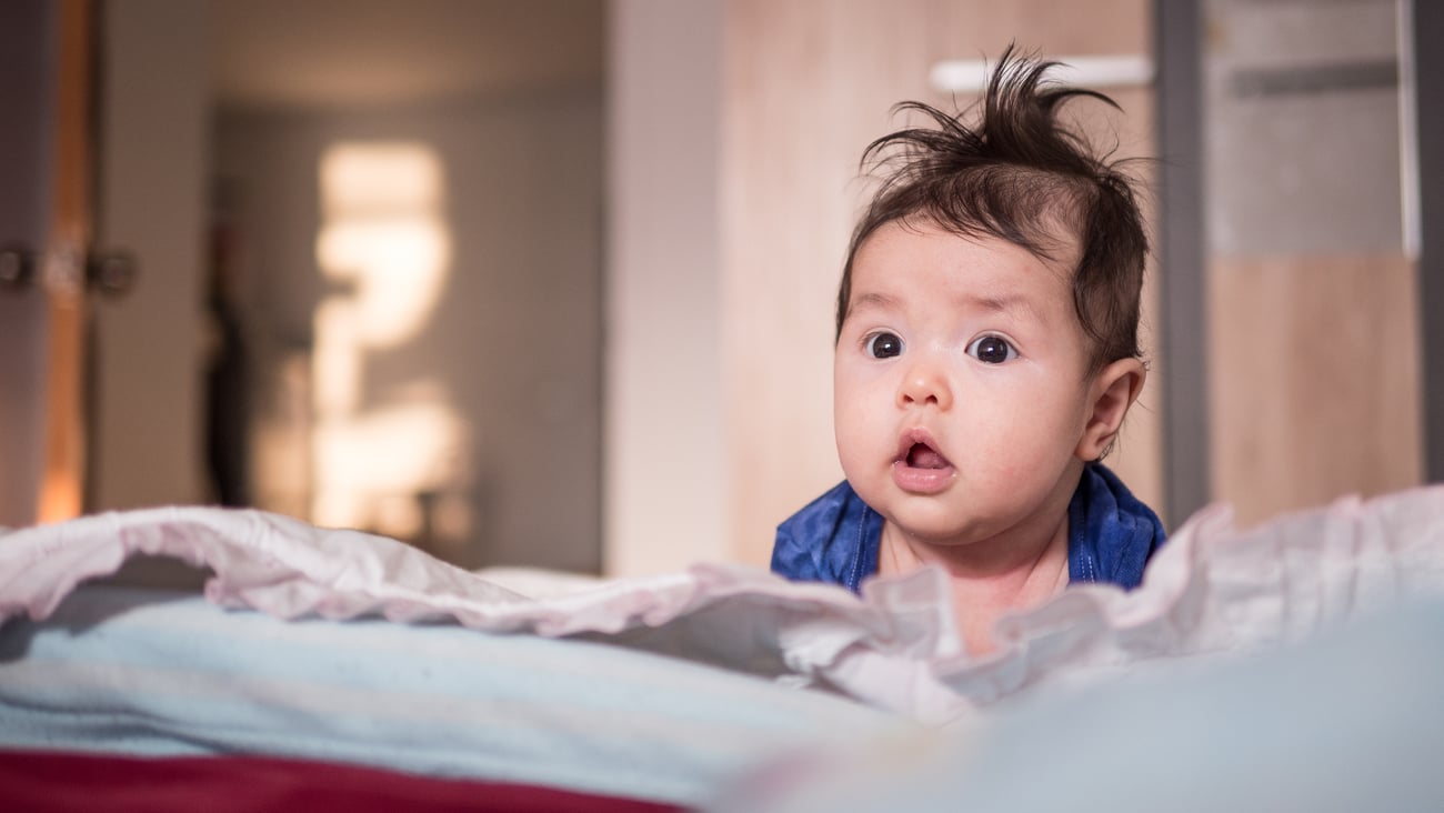 A two-month-old baby girl lying on the bed and looking for something.