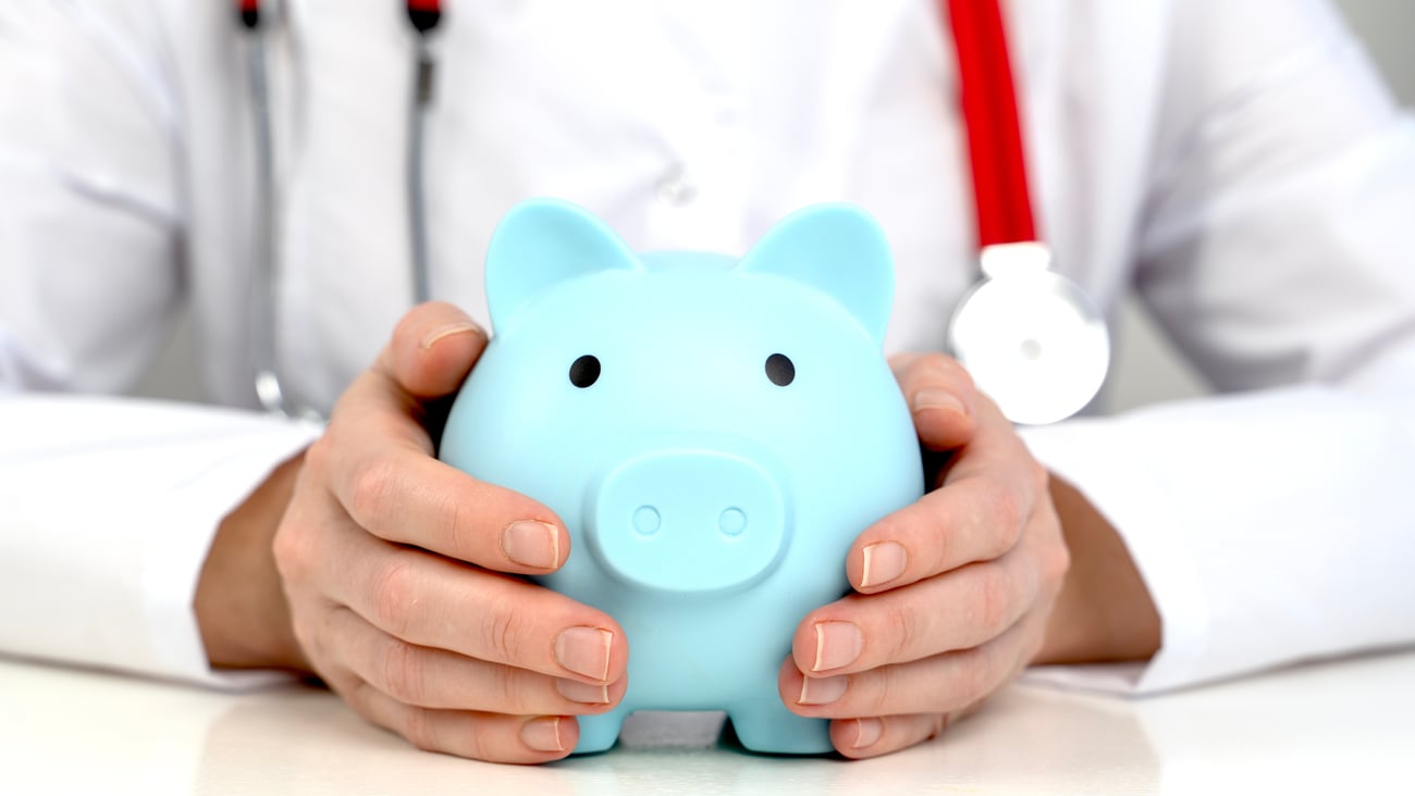 A doctor with a stethoscope holding a piggy bank.