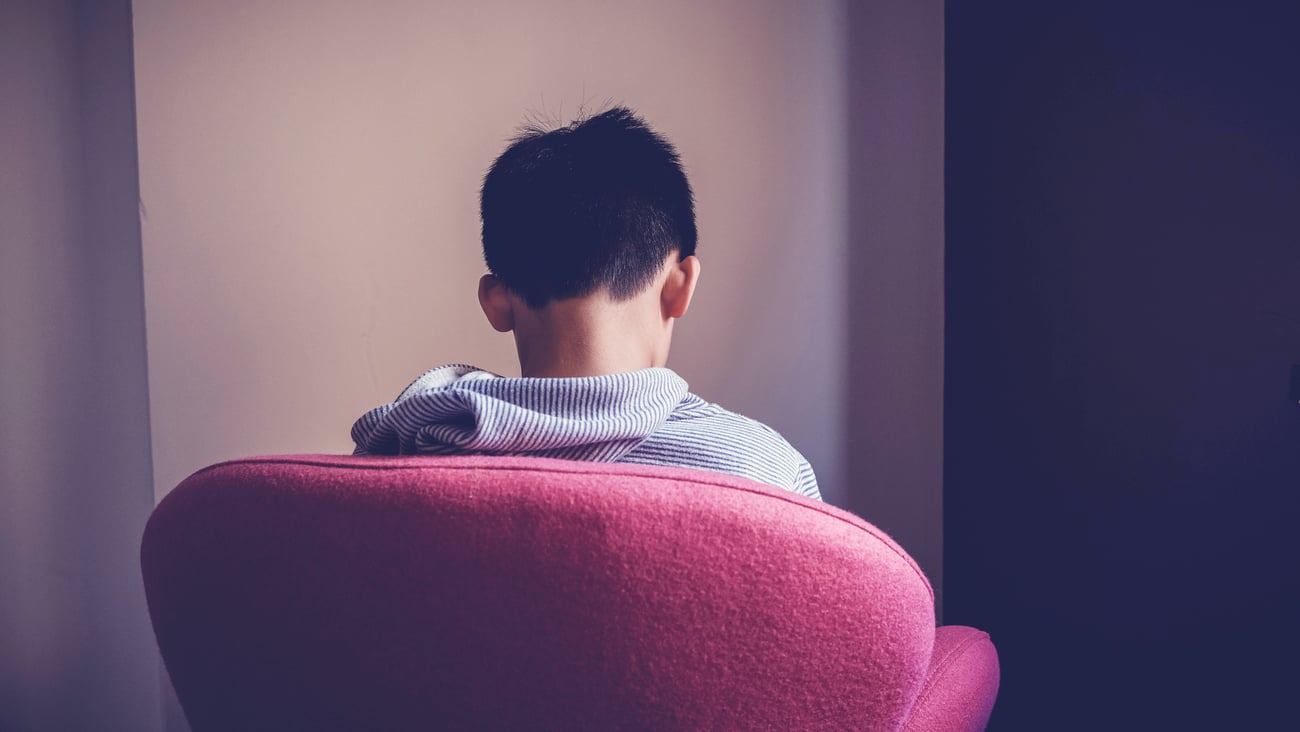 Back of a chair with a tween boy sitting, looking sad