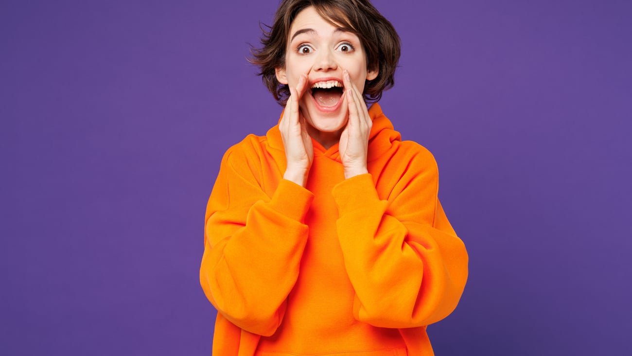 Young woman screaming joyfully in a bright orange sweatshirt
