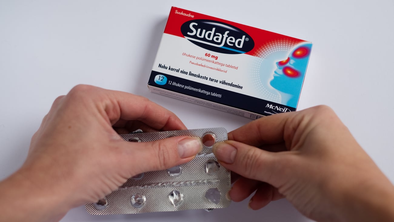 A pair of hands open a box of Sudafed, a prescription medication that contains pseudoephedrine