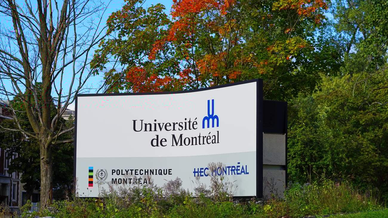 A University of Montreal sign sits amidst a lush, green background during the summer months