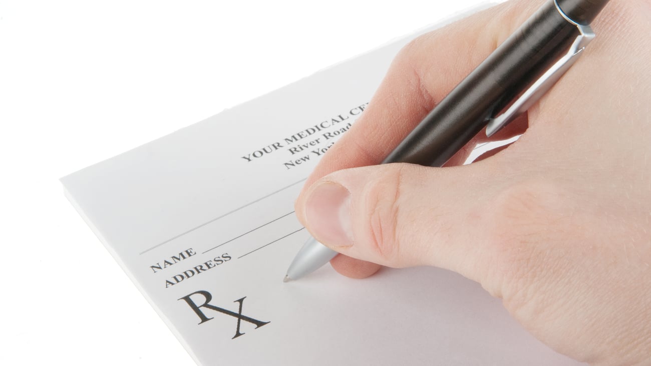 A white person's right hand writes in a prescription pad