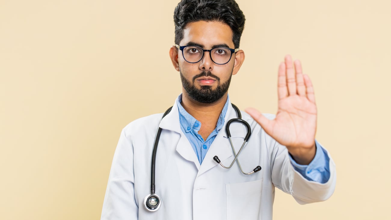 A doctor of South Asian descent holds his hand up in a stop mention, warning against something