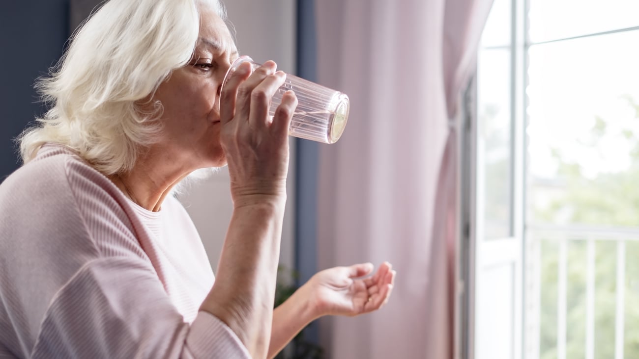 Older white woman in a pink shirt taking a pill with water