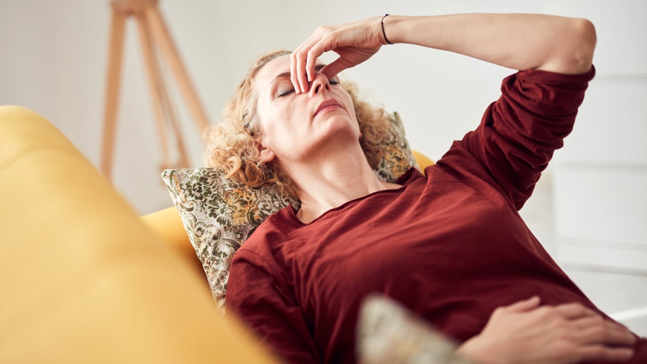 Older white woman leaning back on the couch pinching her nose because she has a sinus headache